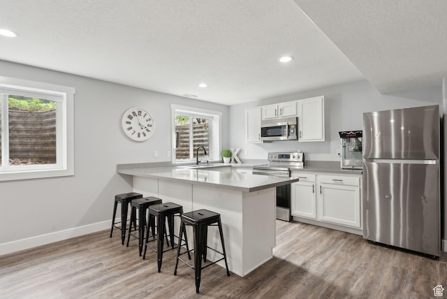 kitchen with stainless steel appliances, a breakfast bar area, plenty of natural light, wood finished floors, and recessed lighting