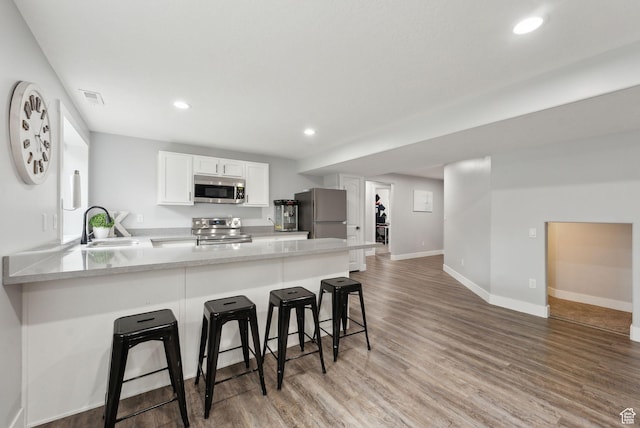 kitchen with appliances with stainless steel finishes, a sink, a peninsula, light wood-style floors, and recessed lighting