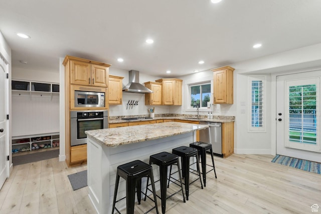 kitchen featuring stainless steel appliances, wall chimney exhaust hood, light brown cabinetry, light wood finished floors, and recessed lighting