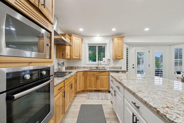 kitchen with stainless steel appliances, a sink, light stone counters, light brown cabinetry, and recessed lighting