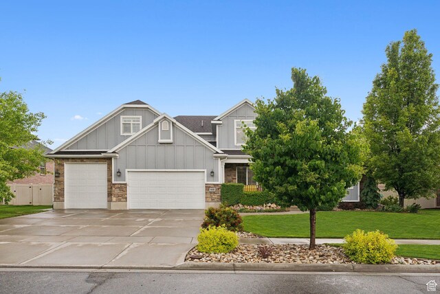 craftsman-style home with board and batten siding, concrete driveway, a front lawn, stone siding, and a garage