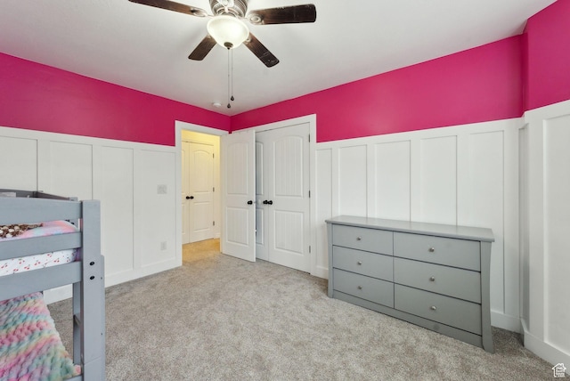 unfurnished bedroom with a decorative wall, carpet flooring, wainscoting, ceiling fan, and a closet