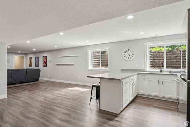 kitchen featuring a sink, open floor plan, a peninsula, baseboards, and a kitchen bar