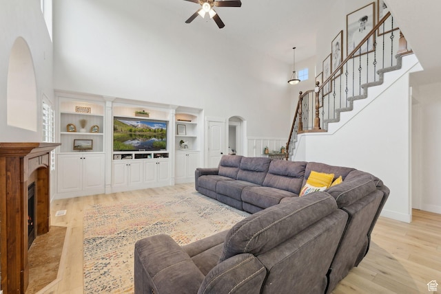 living area featuring a towering ceiling, arched walkways, a ceiling fan, light wood-style flooring, and a fireplace with flush hearth