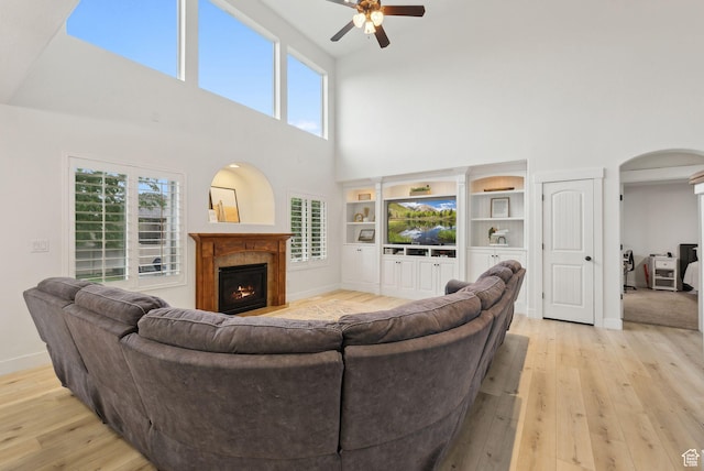 living area featuring a high ceiling, ceiling fan, light wood-style floors, a warm lit fireplace, and arched walkways