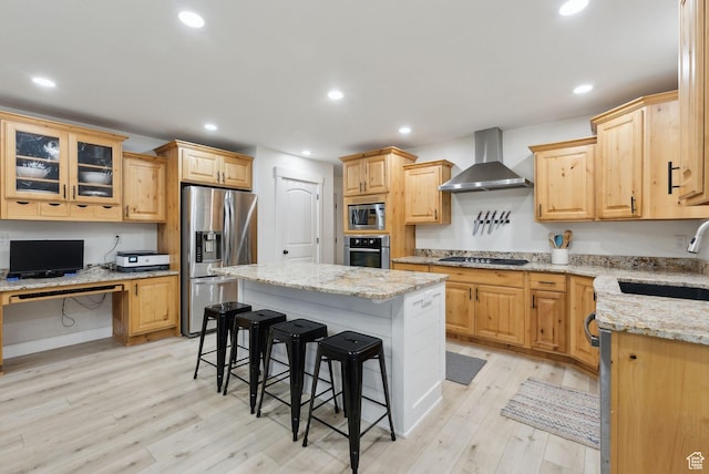 kitchen featuring appliances with stainless steel finishes, a sink, wall chimney exhaust hood, a kitchen breakfast bar, and light wood-style flooring