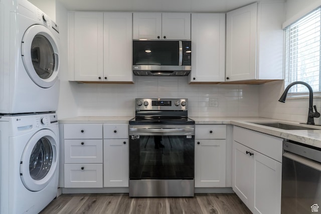 4740 S 3040 W, Taylorsville, UT 84129 - kitchen featuring appliances with stainless steel finishes, a sink, stacked washer and clothes dryer, white cabinets, and decorative backsplash