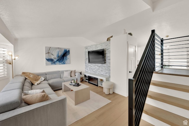living room featuring healthy amount of natural light, stairs, light wood-type flooring, and vaulted ceiling