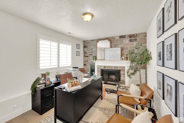 office area featuring a textured ceiling, a stone fireplace, and light wood finished floors