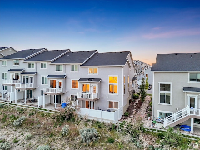 back of property at dusk featuring stucco siding, a residential view, and fence
