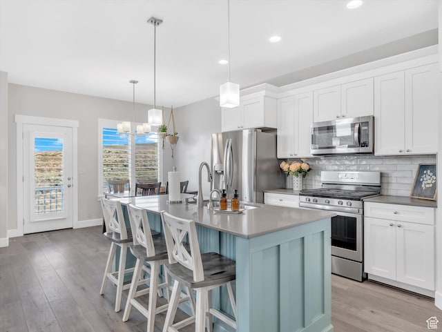kitchen with appliances with stainless steel finishes, tasteful backsplash, light wood-style flooring, a breakfast bar, and an island with sink