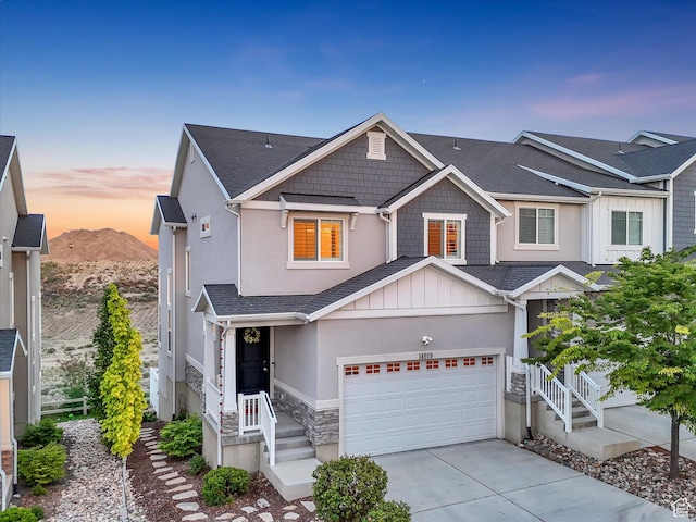 view of front of house with concrete driveway, an attached garage, stone siding, stucco siding, and a mountain view