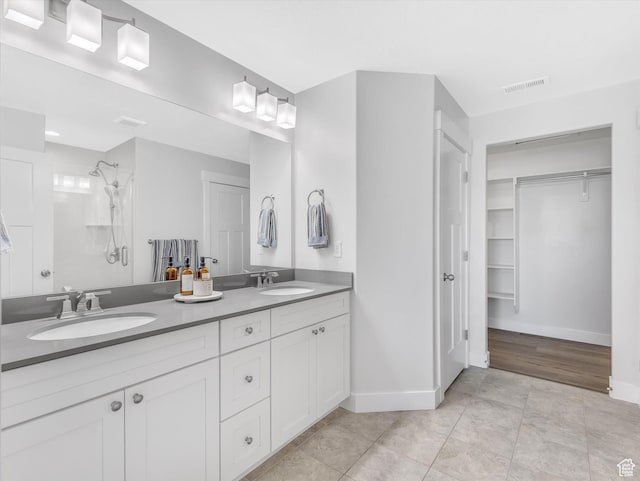 full bath with a shower, baseboards, a spacious closet, and double vanity