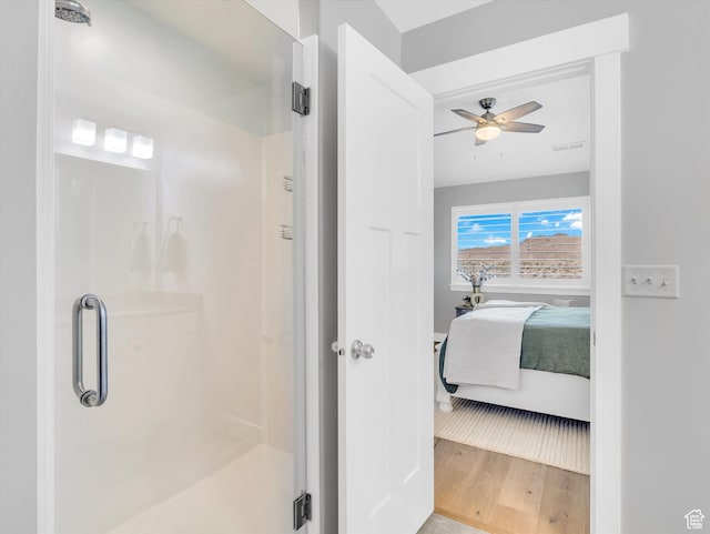 ensuite bathroom with ceiling fan, a stall shower, wood finished floors, and baseboards