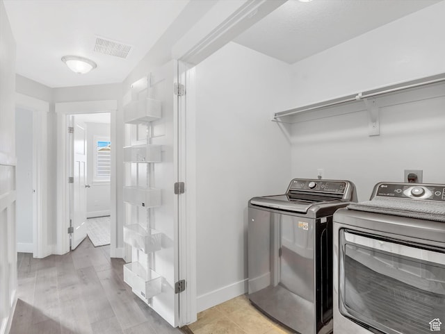 laundry room featuring washing machine and clothes dryer, baseboards, and light wood finished floors