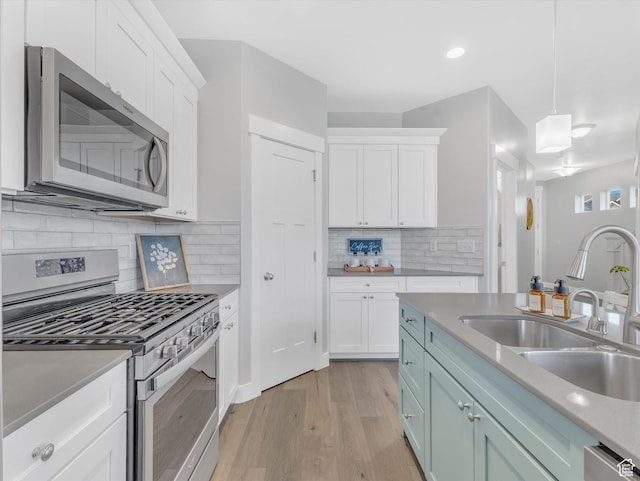 kitchen featuring stainless steel appliances, a sink, white cabinets, light wood-style floors, and recessed lighting