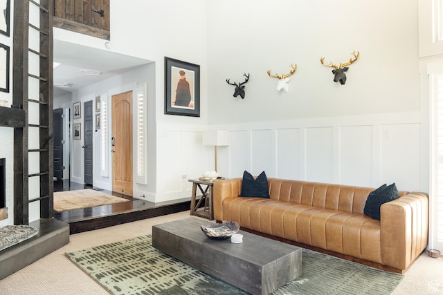 carpeted living room featuring a decorative wall, a fireplace with raised hearth, and wainscoting