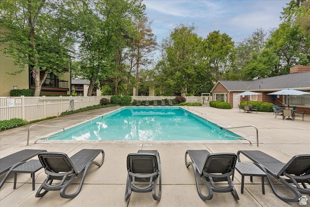 community pool with a patio area, fence, and view of wooded area