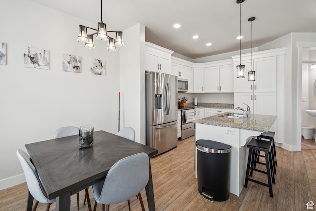 kitchen featuring appliances with stainless steel finishes, a sink, light wood finished floors, white cabinets, and recessed lighting