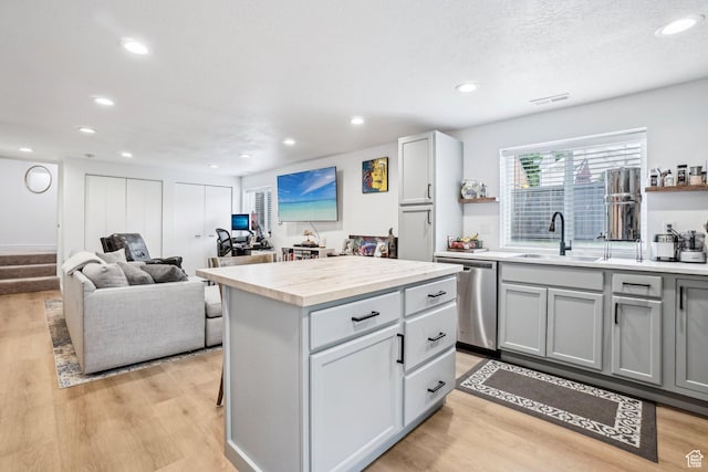 kitchen with stainless steel dishwasher, gray cabinets, a sink, light wood-type flooring, and light countertops