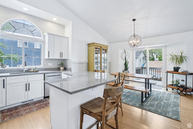 kitchen featuring dishwasher, a sink, a breakfast bar area, light wood finished floors, and lofted ceiling