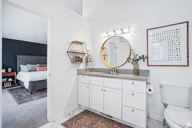 ensuite bathroom with baseboards, toilet, vanity, and marble finish flooring