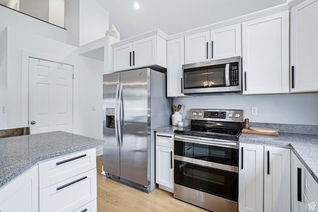 kitchen with appliances with stainless steel finishes, light wood finished floors, white cabinets, light stone counters, and recessed lighting