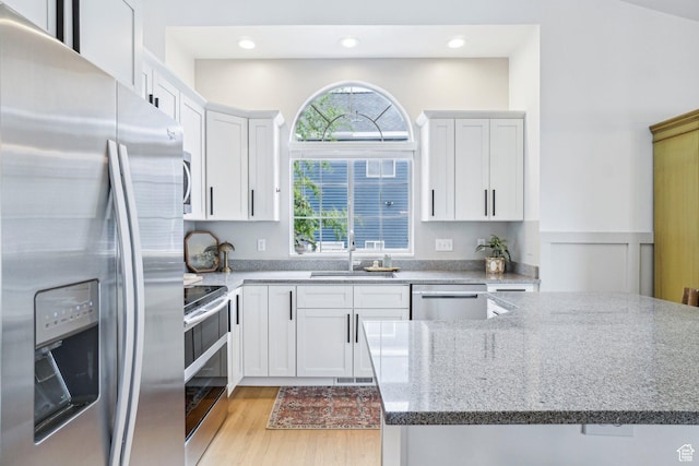kitchen with stainless steel appliances, a sink, light wood-type flooring, white cabinetry, and recessed lighting