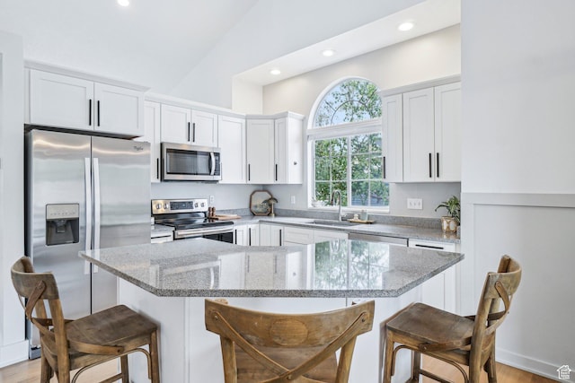 kitchen with appliances with stainless steel finishes, a kitchen bar, a kitchen island, white cabinets, and recessed lighting