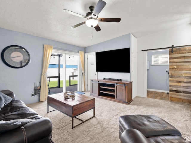 living room with ceiling fan, a barn door, a textured ceiling, and light carpet