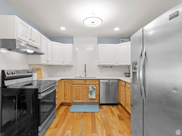 kitchen with stainless steel appliances, under cabinet range hood, a sink, light wood-style floors, and light countertops
