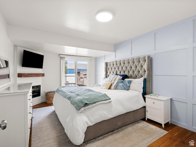 bedroom with dark wood finished floors, a glass covered fireplace, access to exterior, baseboards, and a decorative wall
