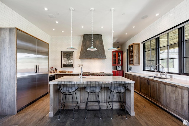 kitchen featuring a sink, stainless steel built in fridge, custom exhaust hood, a kitchen bar, and an island with sink
