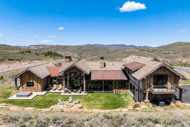 rear view of property featuring a fire pit, a chimney, a mountain view, a patio area, and a yard