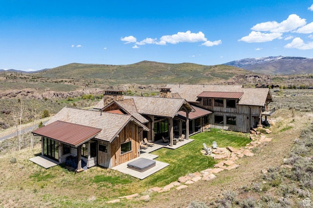 back of house featuring a chimney, a mountain view, a lawn, a patio, and board and batten siding