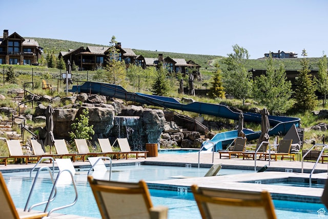 community pool featuring a community hot tub, a water slide, and fence