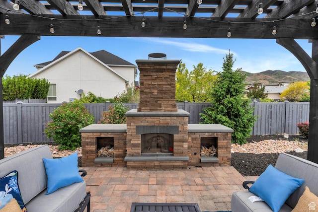 view of patio with an outdoor stone fireplace, a fenced backyard, a mountain view, and a pergola