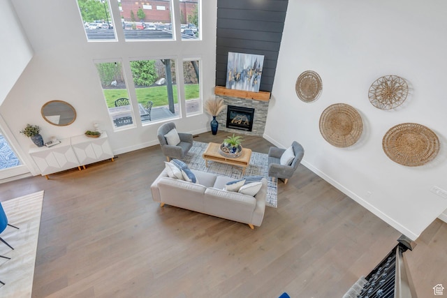living room with a stone fireplace, wood finished floors, baseboards, and a high ceiling