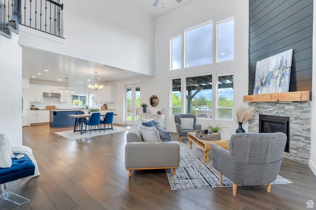 living room featuring wood finished floors, a ceiling fan, a fireplace, a towering ceiling, and a chandelier