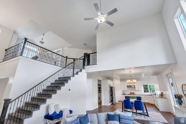 living room with a chandelier, a towering ceiling, dark wood-style flooring, a ceiling fan, and stairs