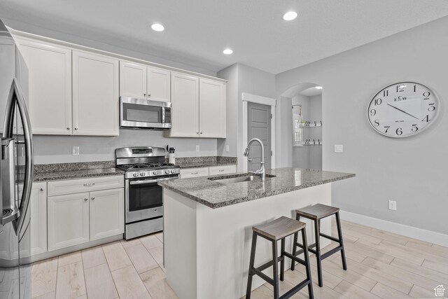 10426 S Kestrel Rise Rd, South Jordan, UT 84009 - kitchen with stainless steel appliances, a sink, arched walkways, dark stone countertops, and white cabinetry