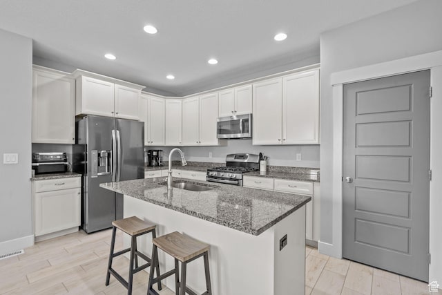 kitchen with appliances with stainless steel finishes, a sink, recessed lighting, dark stone counters, and white cabinetry