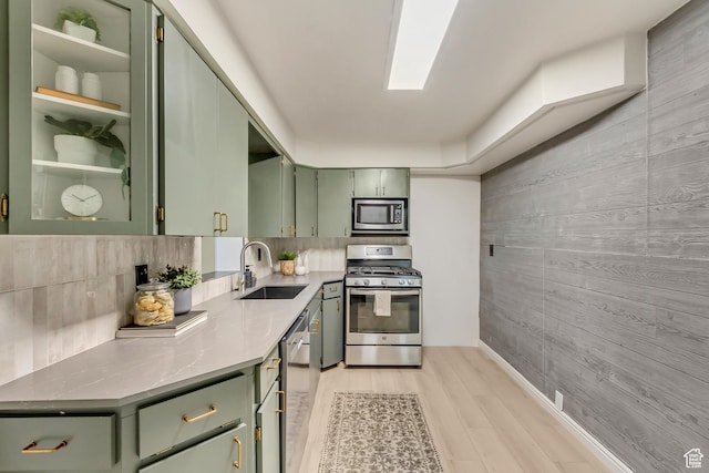 kitchen featuring green cabinets, stainless steel appliances, a sink, wood walls, and light countertops