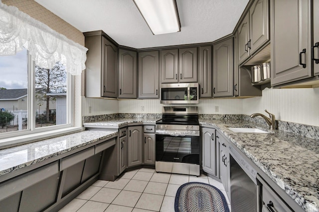 kitchen with stainless steel appliances, a sink, gray cabinets, light tile patterned floors, and light stone counters
