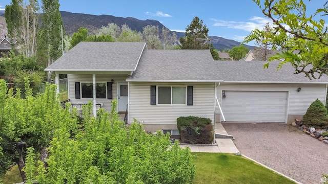 view of front of property featuring an attached garage, gravel driveway, a mountain view, a shingled roof, and a front yard