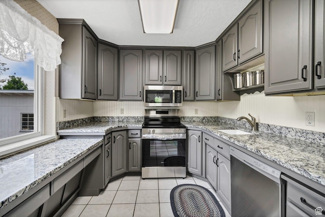 kitchen with stainless steel appliances, a sink, light stone counters, light tile patterned floors, and gray cabinets