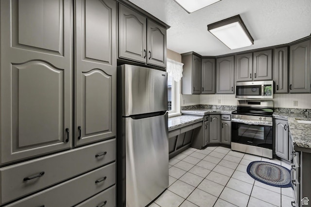kitchen with appliances with stainless steel finishes, light tile patterned floors, light stone countertops, and gray cabinetry