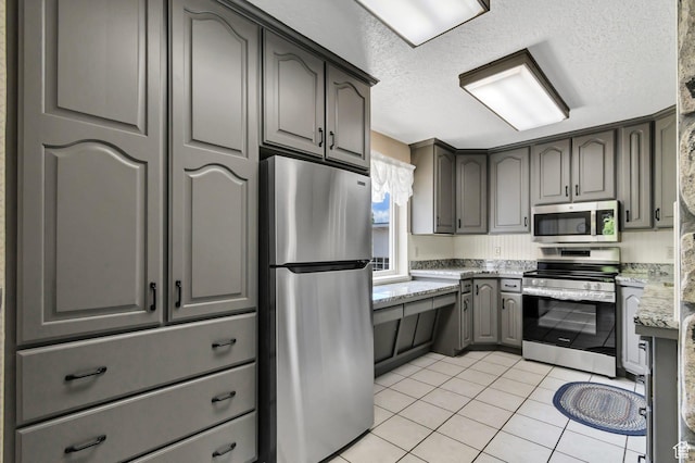 kitchen featuring appliances with stainless steel finishes, gray cabinets, light tile patterned floors, a textured ceiling, and light stone countertops