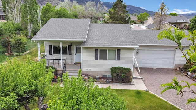 view of front of property with a porch, a garage, a shingled roof, a mountain view, and gravel driveway