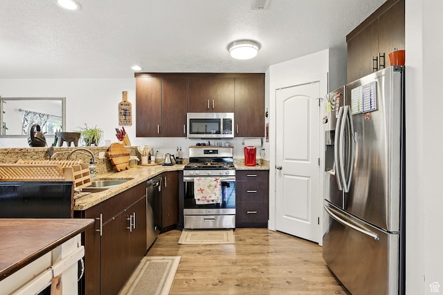 kitchen featuring stainless steel appliances, a sink, dark brown cabinets, light wood-style floors, and a textured ceiling